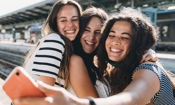 Junge Frauen die gemeinsam, auf einem Bahnsteig, ein Selfi aufnehmen.