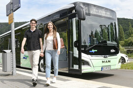 Ein Pärchen siegt an einer Haltestelle aus einem Bus aus. 