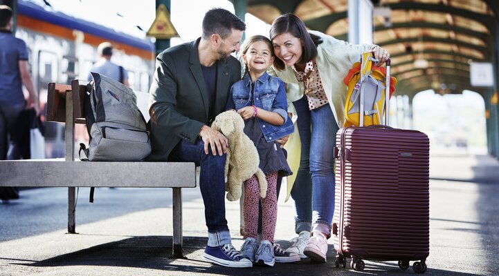 Eine junge Familie, aus Vater, Mutter ein kleinen Mädchen sitzen am Kasseler Hauptbahnhof mit Koffern
